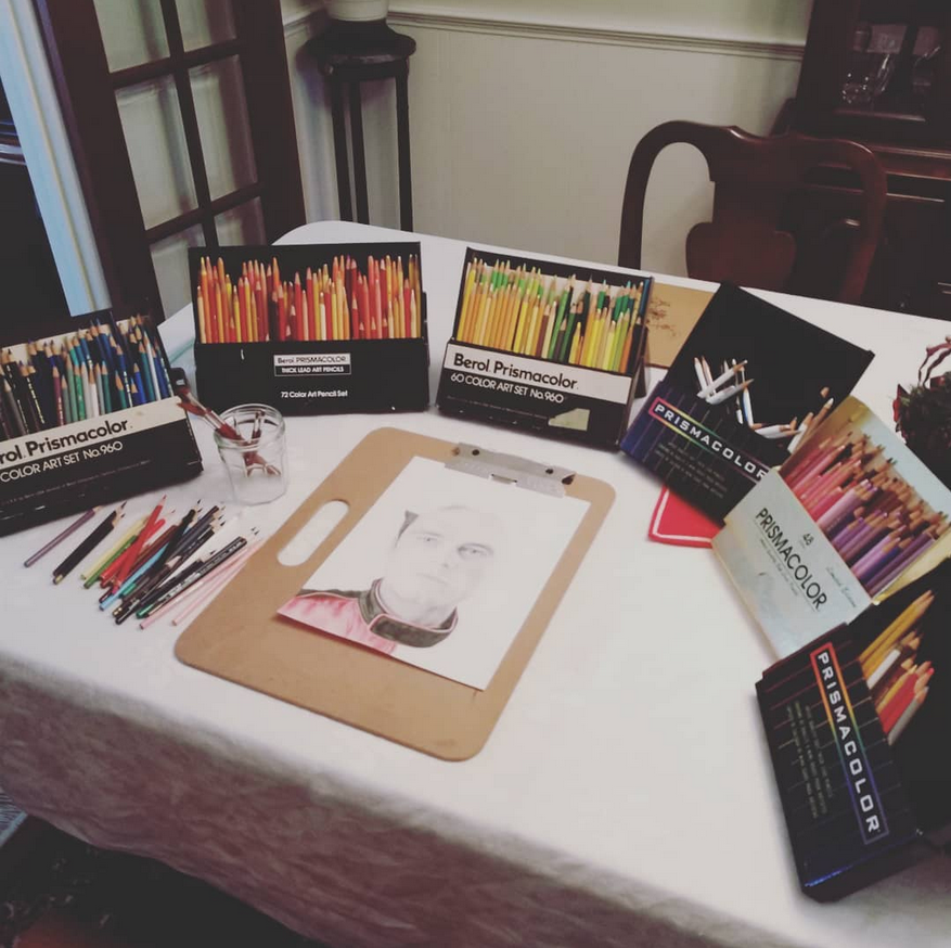 table with artwork surrounded by boxes of colored pencils